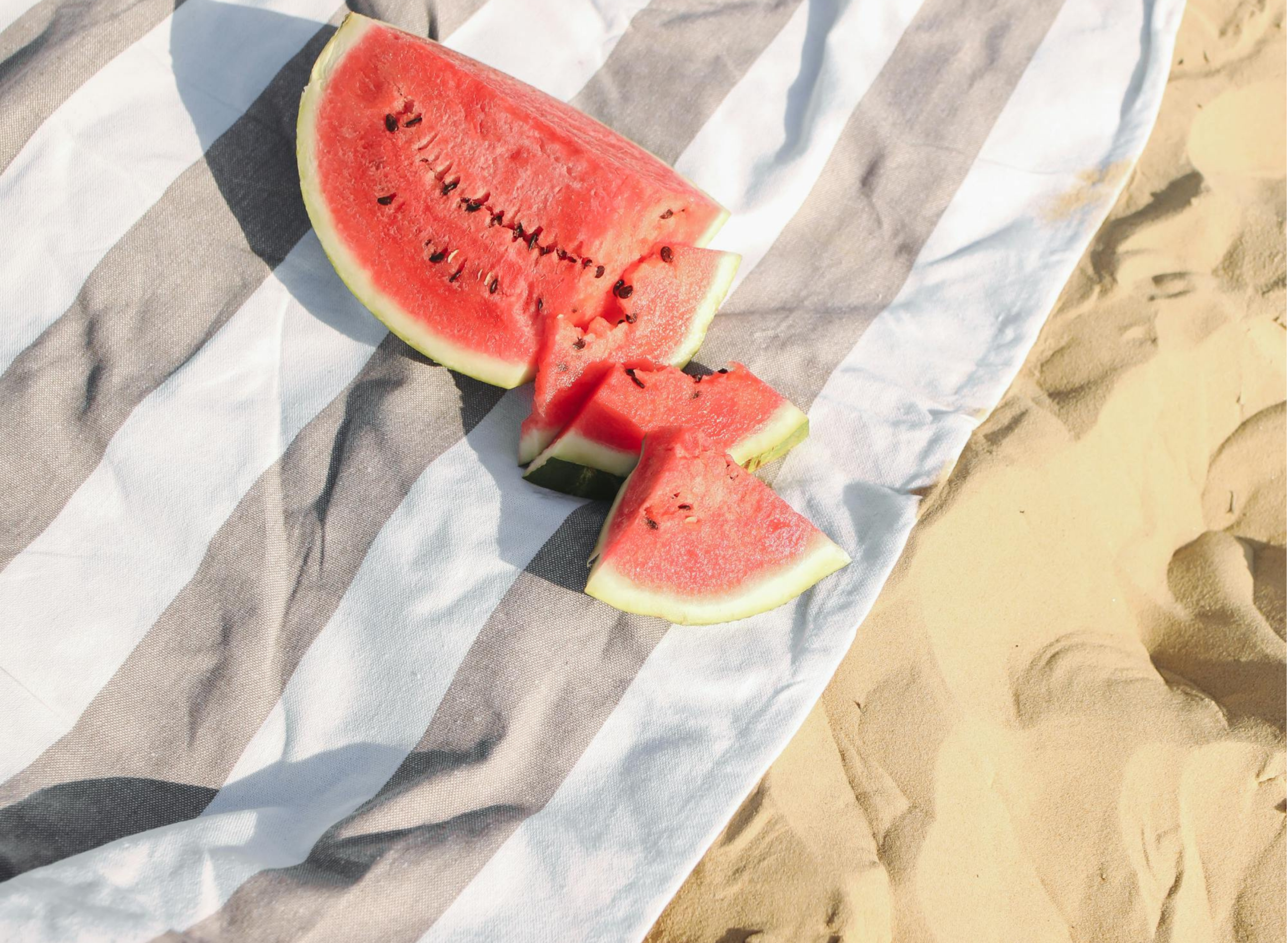 Fresh watermelon slices on a striped beach towel in the sand