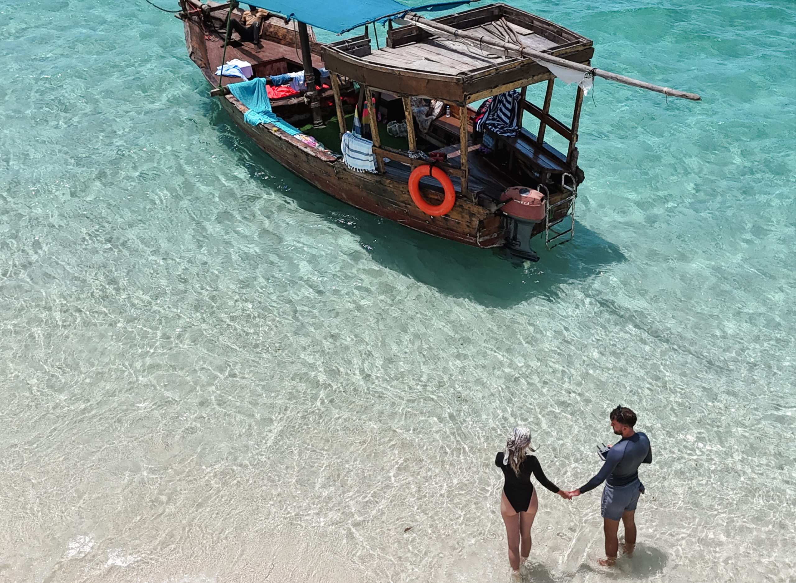 Couple walking in shallow water toward a traditional wooden dhow in Zanzibar