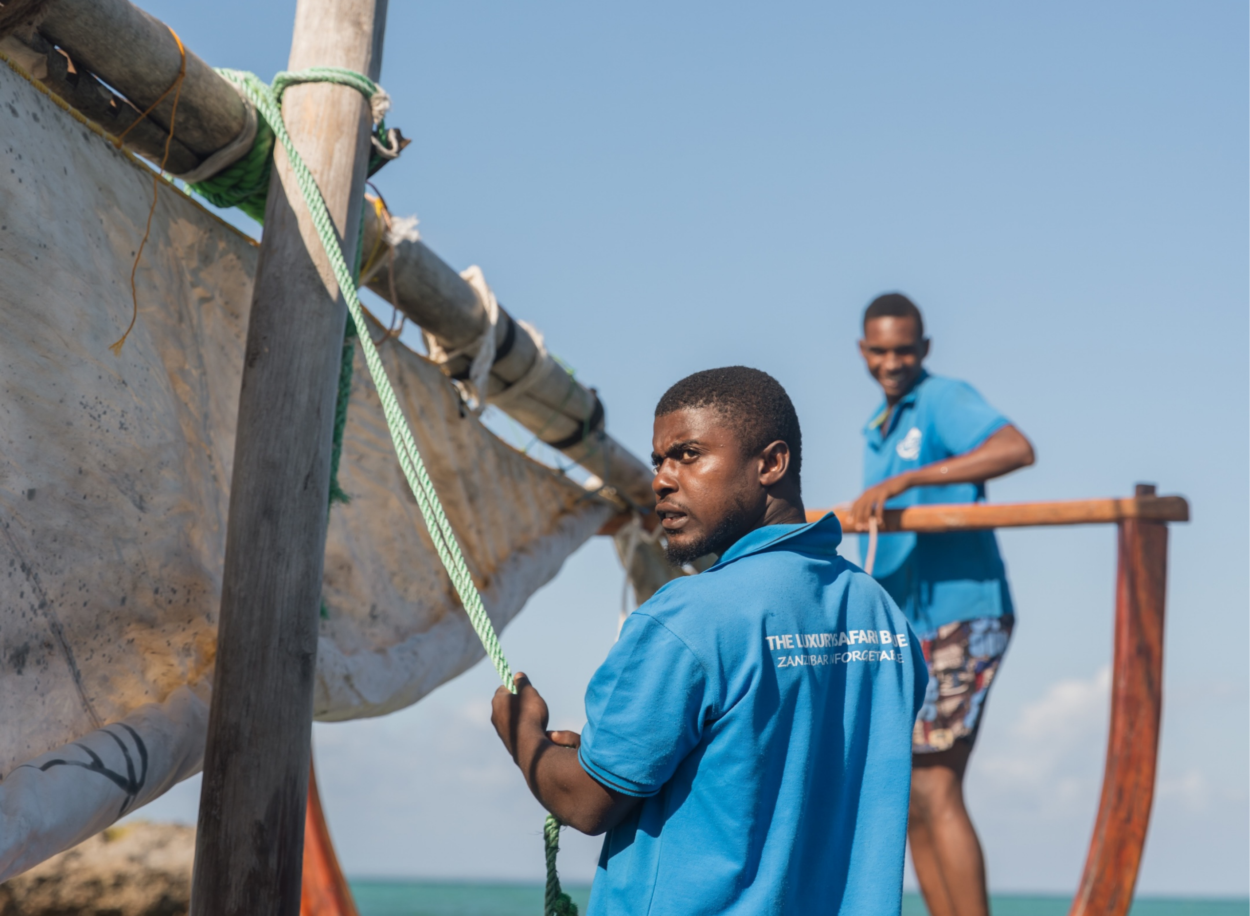 Local crew raising the sail on a traditional wooden dhow in Zanzibar